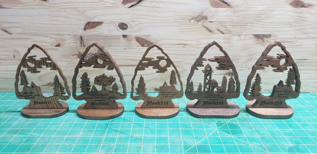 Five arrowhead-shaped awards with forest scenes, on stands